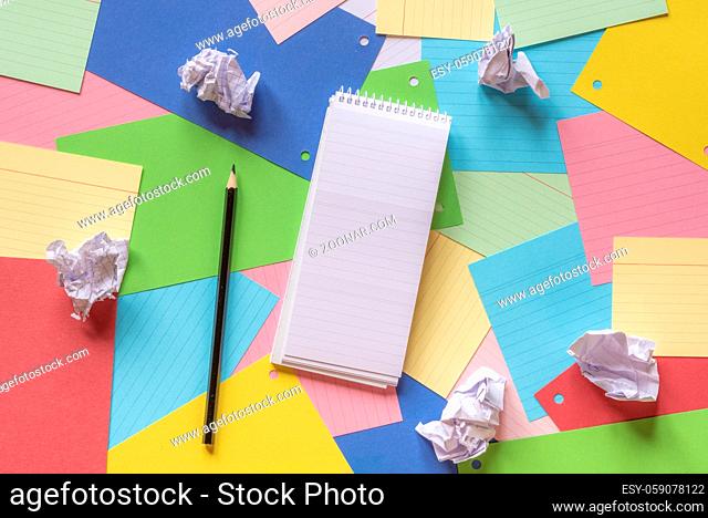 Office workspace with an empty notebook, crumpled paper, and pencil on a colorful background