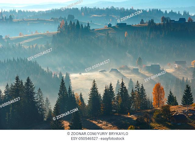 First rays of sun through fog on slopes. Morning autumn Carpathian village landscape (Ivano-Frankivsk oblast, Ukraine)