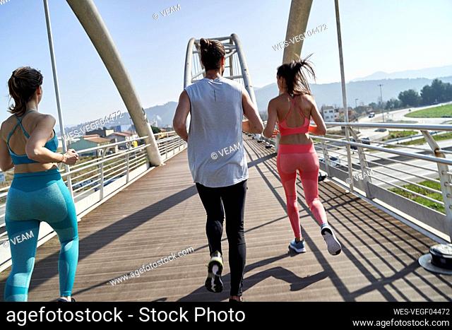 Male and female friends jogging on bridge during sunny day