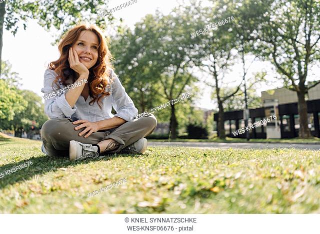 Smiling redheaded woman sitting on grass verge