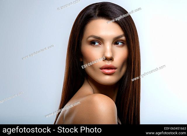 beautiful young woman with natural glowing makeup and long straight hair. beauty shot on gray background. hand touching face. copy space