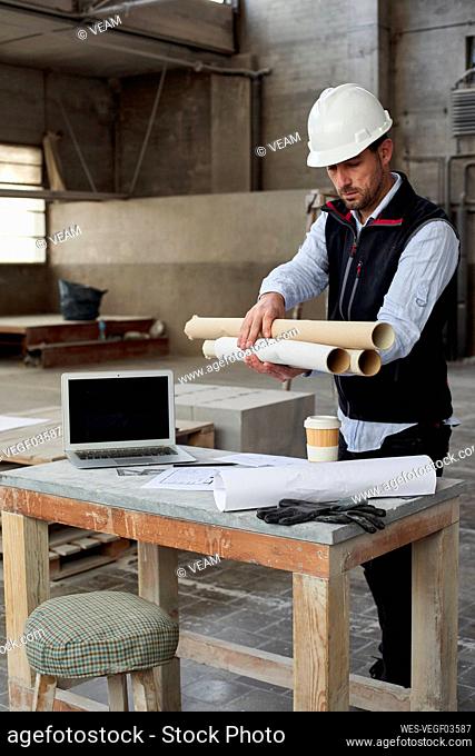 Male engineer holding blueprints while standing at table in building