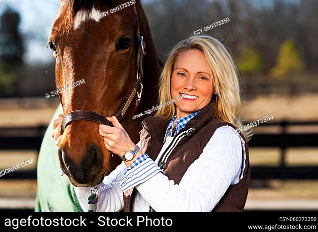 A blonde female with horses in an equestrian environment