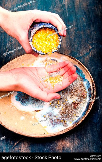 Close shot of female hands putting sea salt from bowl on pottery plate
