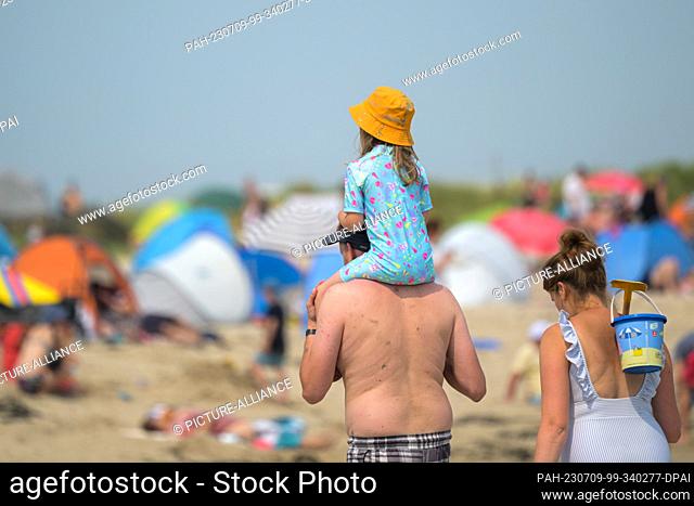 09 July 2023, Lower Saxony, Schillig: A pair of parents are on the beach at Schillig in summer temperatures, while their daughter sits on her father's shoulders