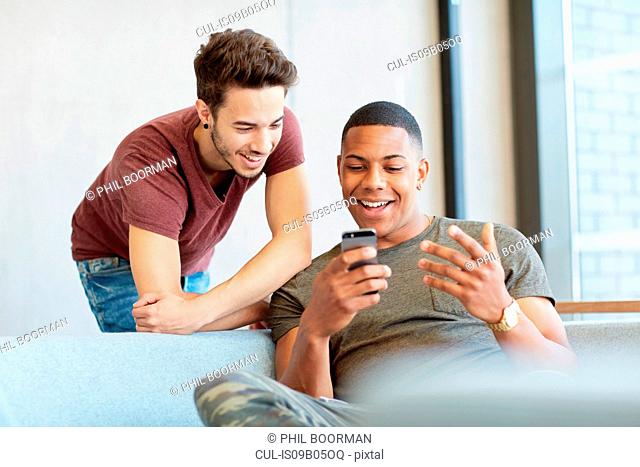 Two young male students in study space sharing text messages at higher education college