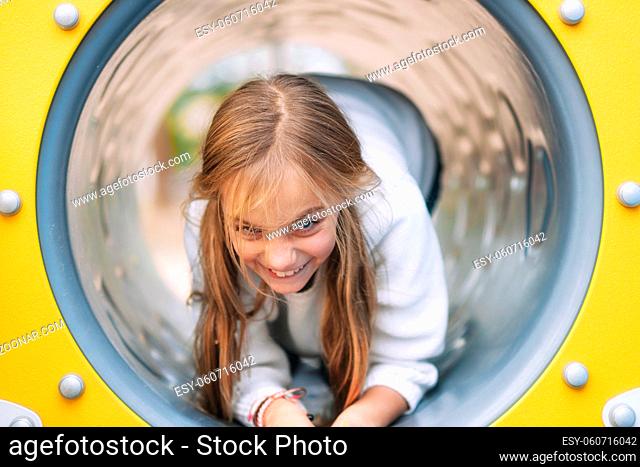 Pretty, little girl, having fun, crawling on pipe on children playground