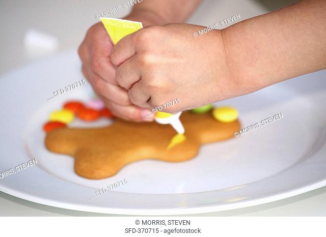 Child's hands decorating a gingerbread man with writing icing