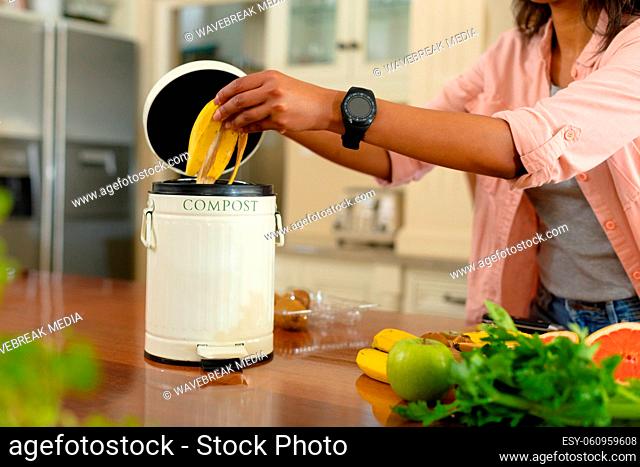 Midsection of young african american woman putting banana peel in compost bin at home