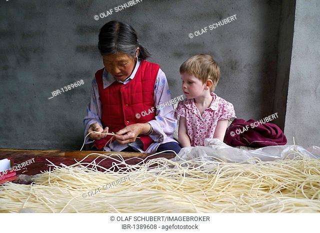 Encounters in China, young European girl watching on old Chinese woman making incense sticks, Moxi, Hailuogou, Sichuan, China, Asia