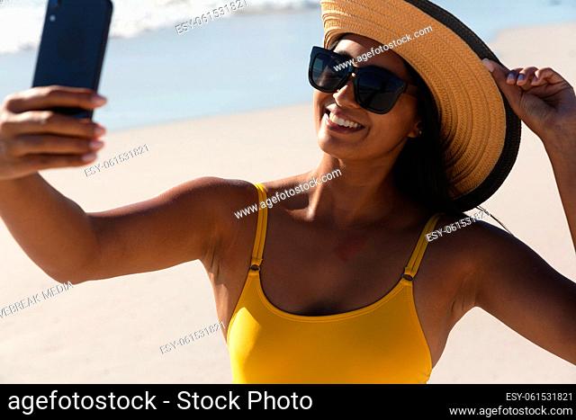Smiling mixed race woman on beach holiday taking selfie