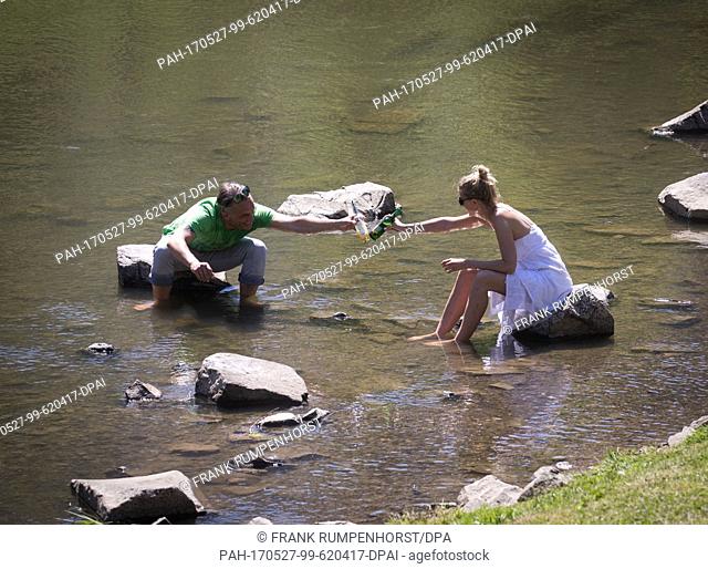 dpatop - Two day trippers sit on stones in the Nidda River and raise their glasses in Bad Vilbel, Germany, 27 May 2017. Photo: Frank Rumpenhorst/dpa