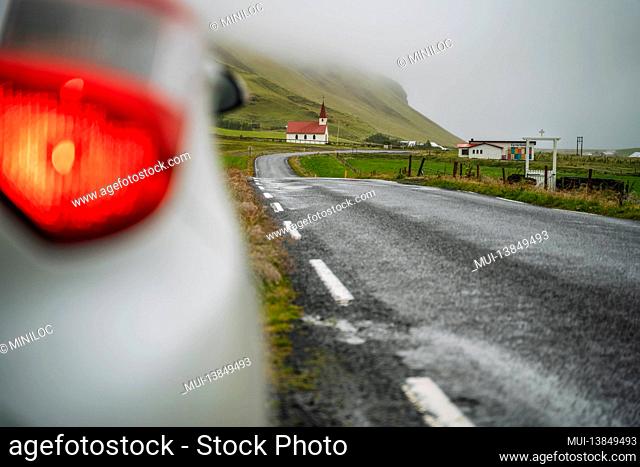 Car stoped on the road with view of typical rural Icelandic Church with red roof in Vik region. Iceland