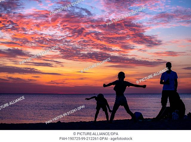 25 July 2019, Mecklenburg-Western Pomerania, Timmendorf (Poel): Swimmers watch the sunset on the beach of Timmendorf on the island of Poel