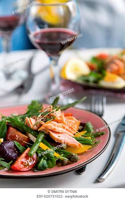 salad with salmon and verdure in plate on table with blue chair background