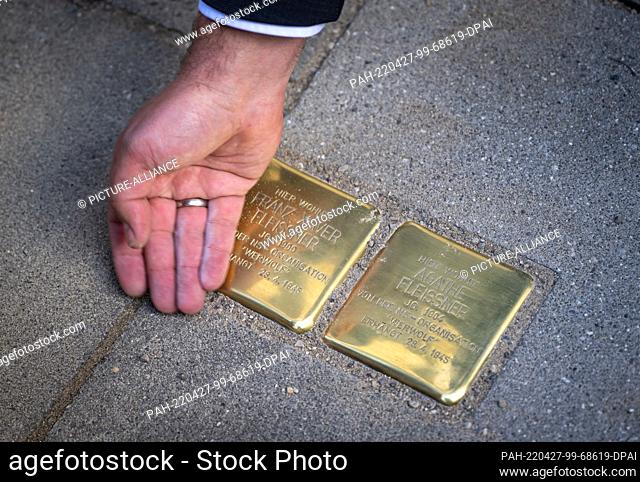 27 April 2022, Bavaria, Penzberg: The ""Stolpersteine"" made by artist Gunter Demnig are touched by a hand shortly after being laid on a sidewalk in front of a...