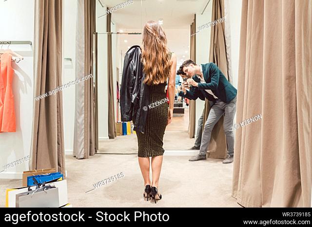 Man making phone photo of his wife with her new dress in fashion store