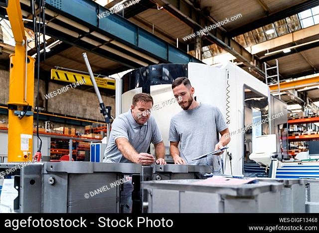 Male engineer examining product standing by young coworker in industry