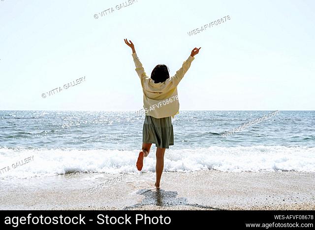 Woman with arms raised standing at beach during sunny day
