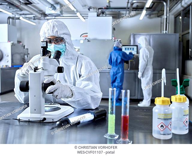 Chemists working in industrial laboratory, wearing protective clothing, using microscope