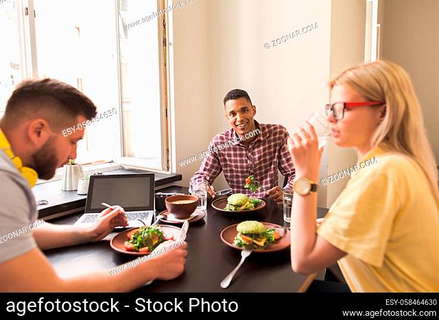 Portrait of happy businessman looking at camera while his partners communicating about business in vegan restaurant or cafe. Team work concept