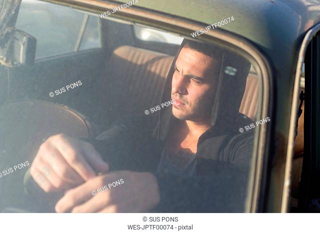 Young man sitting in a broken car on a scrapyard