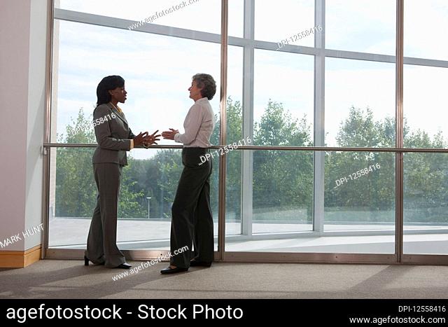 Two business women talking together in the corridor of a workplace