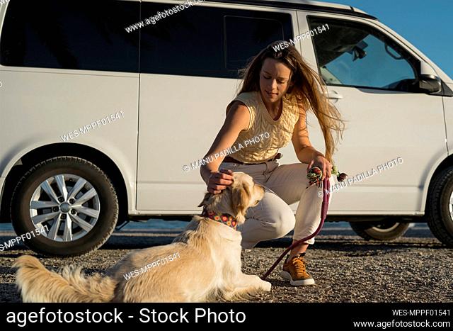 Woman stroking dog by camper van during weekend
