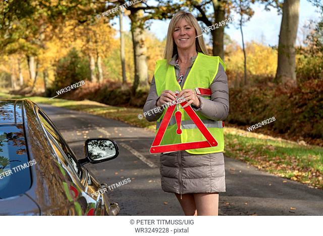 Female motorist putting out a reflective safety triangle following a roadside breakdown