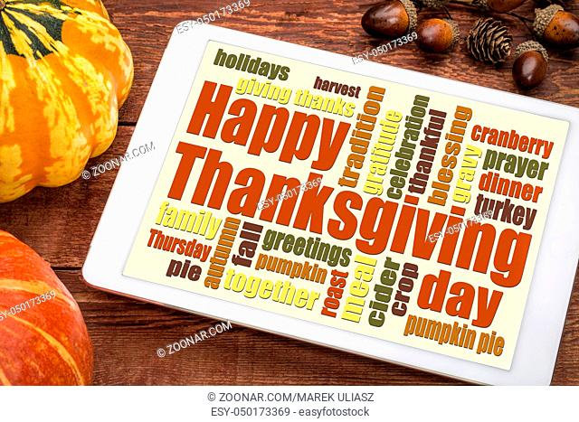Happy Thanksgiving word cloud on a digital tablet with pumpkin and acorn decoration