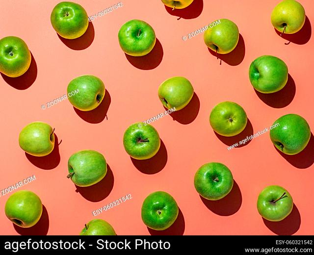 Green apples on orange or coral pink background pattern. Colorful fruit frame. Flat lay or top view, Hard light. Creative concept