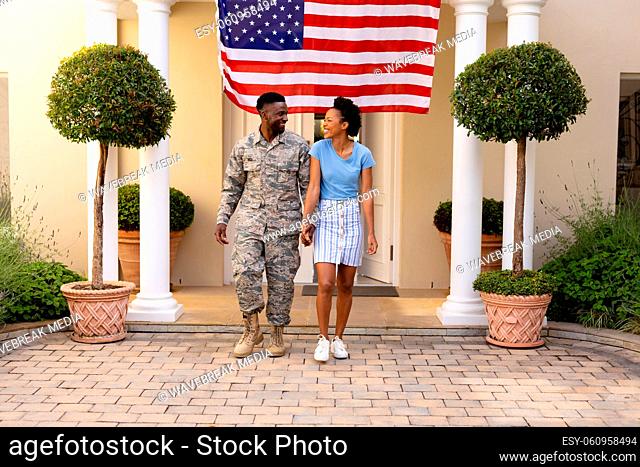 Full length of smiling african american military man holding hands with woman against usa flag