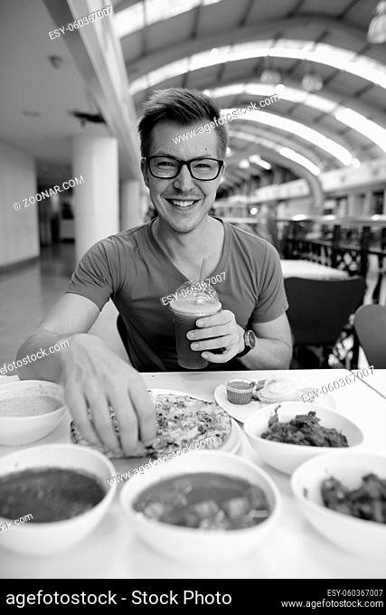 Portrait of young handsome tourist man enjoying Indian cuisine at the restaurant in black and white