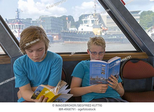 Young people on a language trip read an English travel guide on the Elbe ferry, Hamburg, Germany, Europe