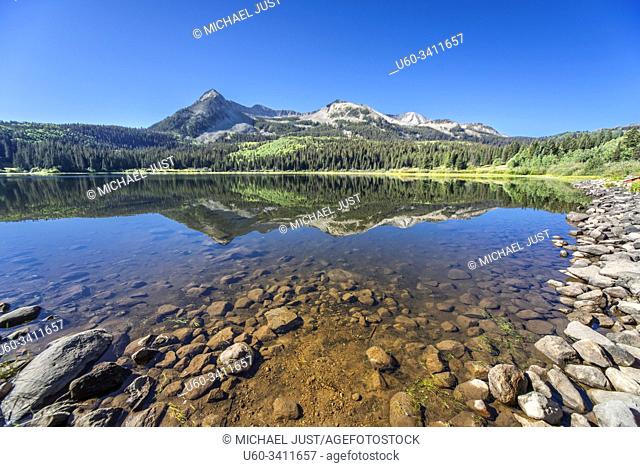 The surrounding forest and mountains are reflected in the still Lost Lake in Colorado