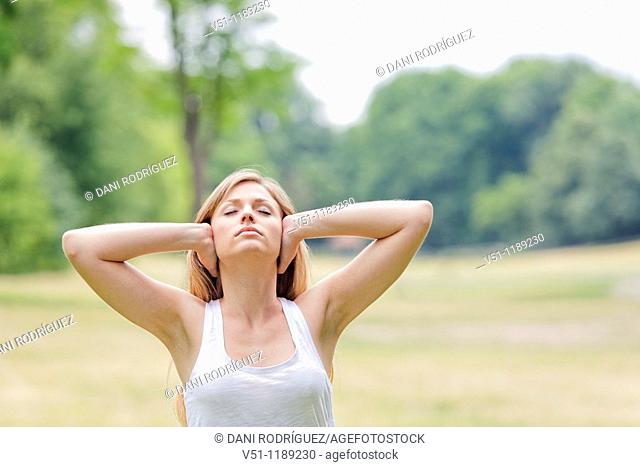 Portrait of a blonde woman covering her ears in the park