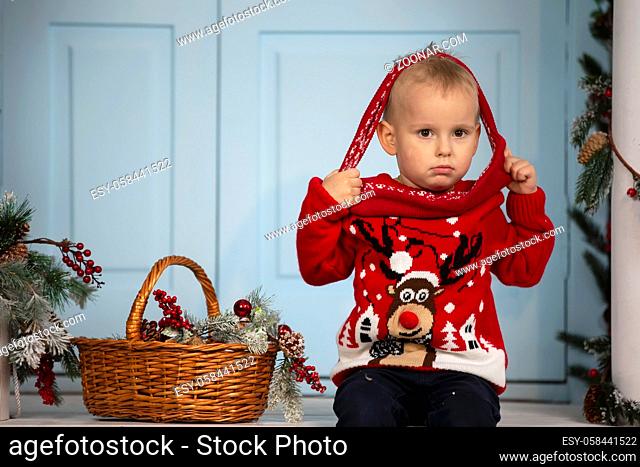 Happy little boy in christmas. A funny child sits with a basket filled with Christmas decorations