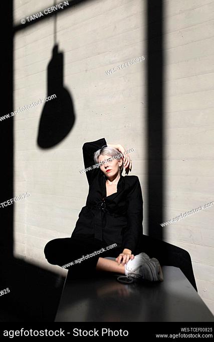 Stylish female professional wearing elegant suit sitting with sunlight and shadow in background at office