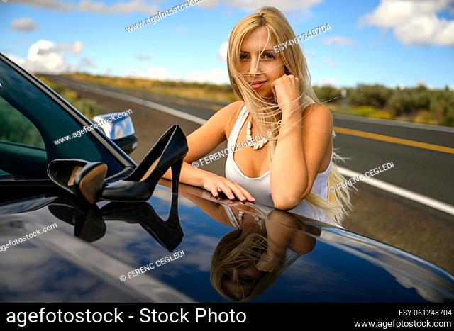 Absolute freedom. Pretty young woman stopped her car in the middle of nowhere, took her high heel shoes off and put them on the engine hood