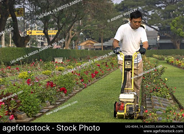 Gardener uses trimmer to tidy grass edges Don Rak Kanchanaburi War Cemetery Thailand