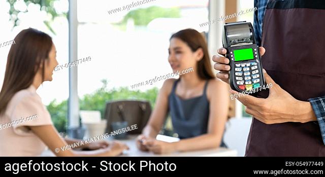 Panoramic close up of waiter hand hold credit card reader for contactless payment with customers in restaurant background