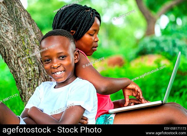 Close up portrait of happy African kids under tree playing on laptop