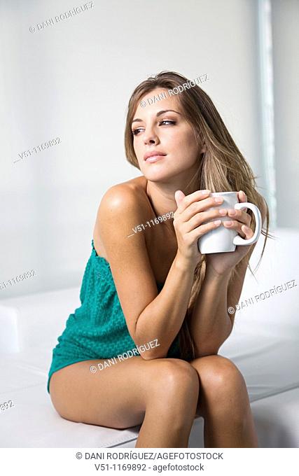 Beatiful pensive blonde woman enjoying a drink at home