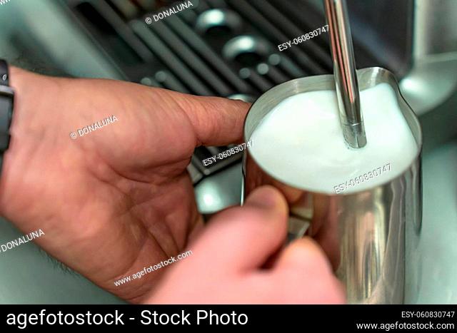 A man whisks milk for a latte in a steel jug