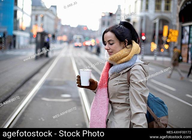 Beautiful woman with disposable cup crossing road at street during winter