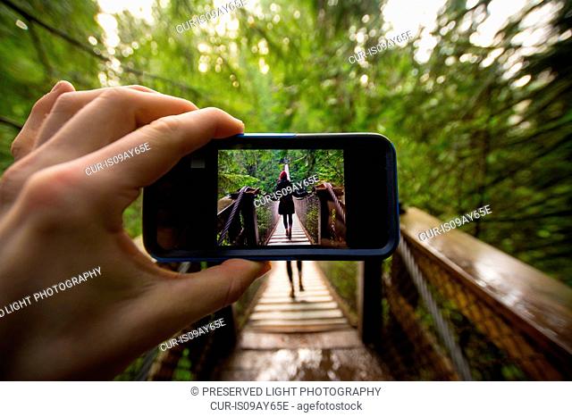 Man hand holding smartphone with image of woman on Lynn canyon suspension bridge, North Vancouver, British Columbia, Canada