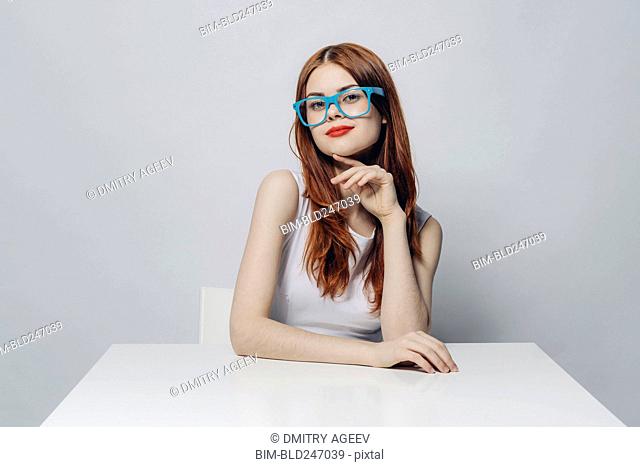 Pensive Caucasian woman sitting at table wearing blue eyeglasses