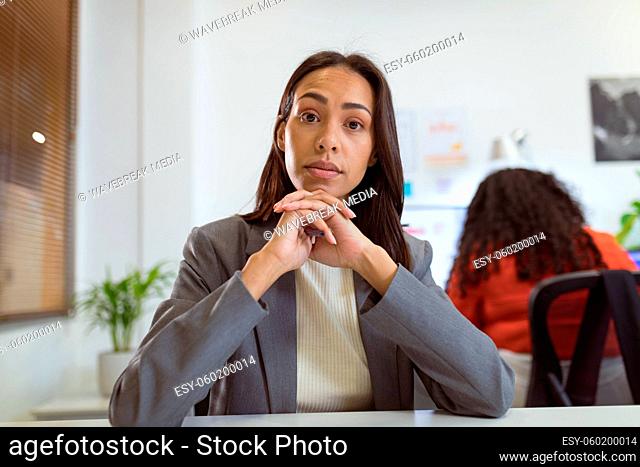 Thoughtful biracial businesswoman sitting at desk making video call in modern office