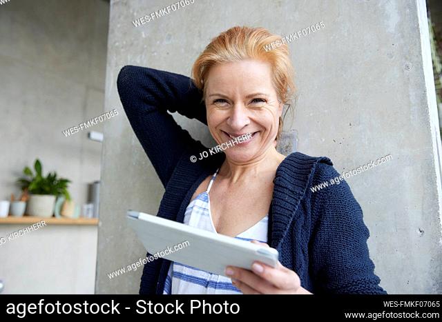Happy woman with digital tablet against column at home