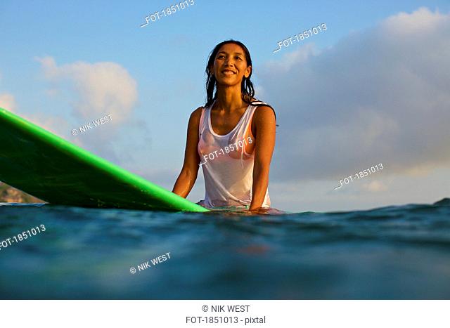 Smiling, confident female surfer waiting on surfboard in ocean